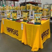 HIPPEAS roadshow sampling table with branded tablecloth and product displays inside a Costco warehouse.